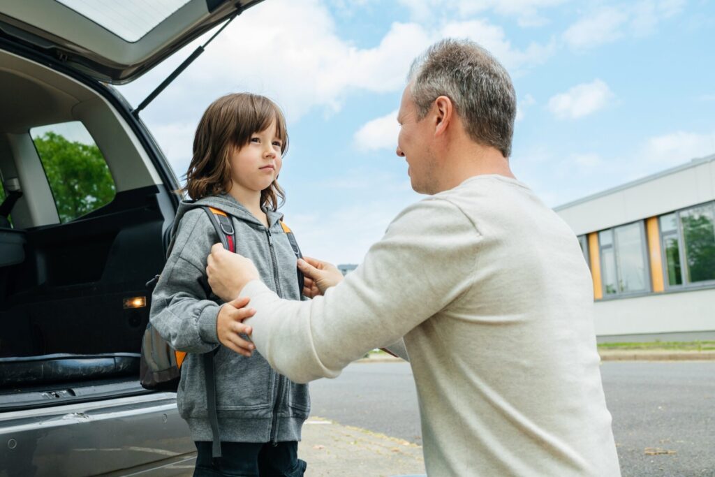 A father helps his son to put on a backpack. The child is happy to go back to school or kindergarten